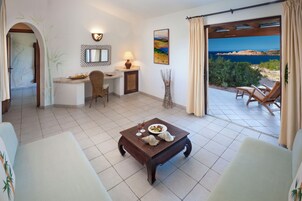 Una habitación con una mesa de comedor dispuesta con platos y vasos, una silla, un escritorio con una lámpara, un cuadro y vistas al mar a través de una ventana.