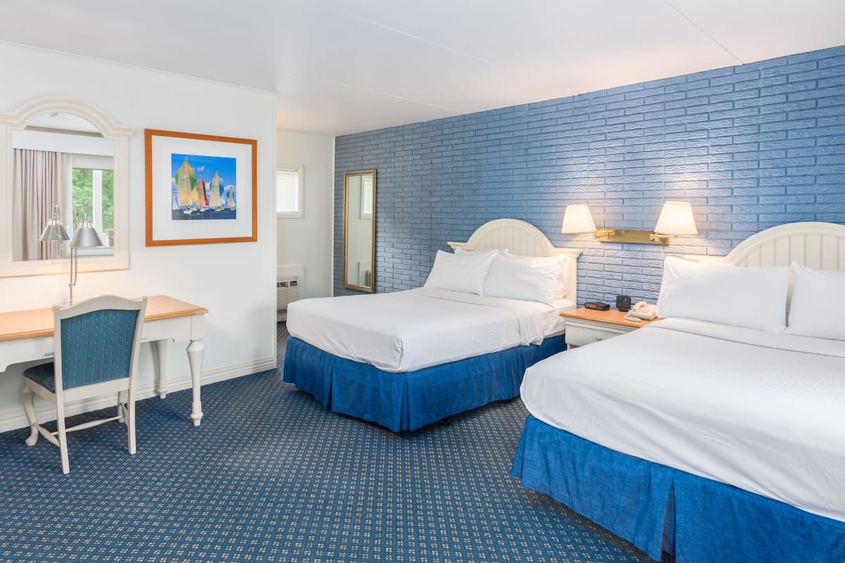 A hotel room with two beds, a desk, and a chair.