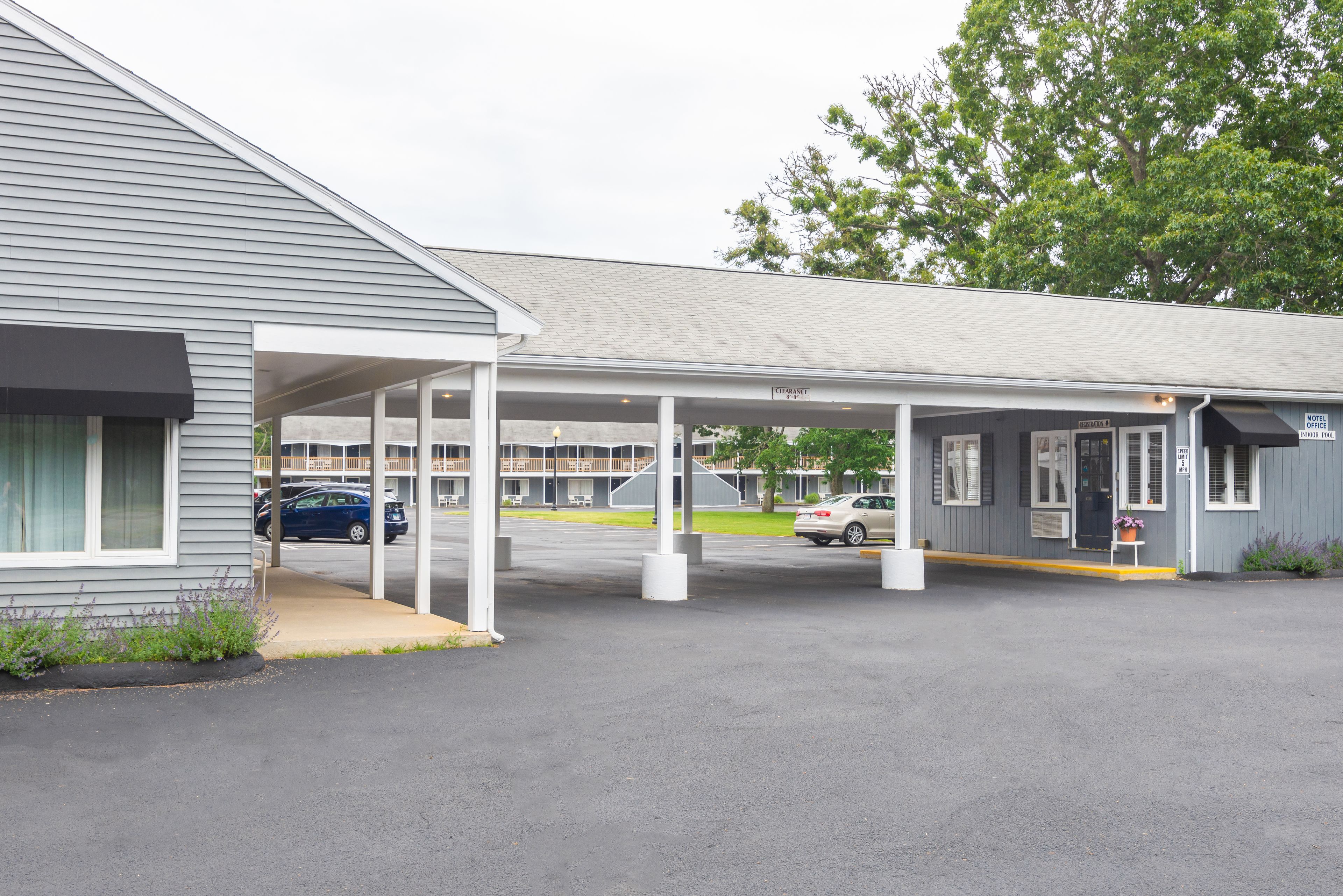 Un motel doté d’un parking couvert, un bâtiment avec une enseigne indiquant le bureau du motel, et une voiture garée sur le parking.