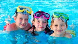 Three children in a swimming pool wearing different colored goggles. - Ocean Park Inn (Eastham)