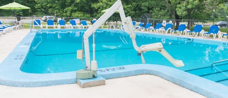 Una piscina con agua azul, rodeada de sillas reclinables azules y blancas, y un trampolín.