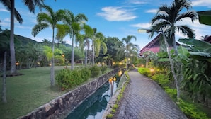A pathway with a water channel, surrounded by greenery and palm trees. - Long Bay Resort (Ko Pha-ngan)