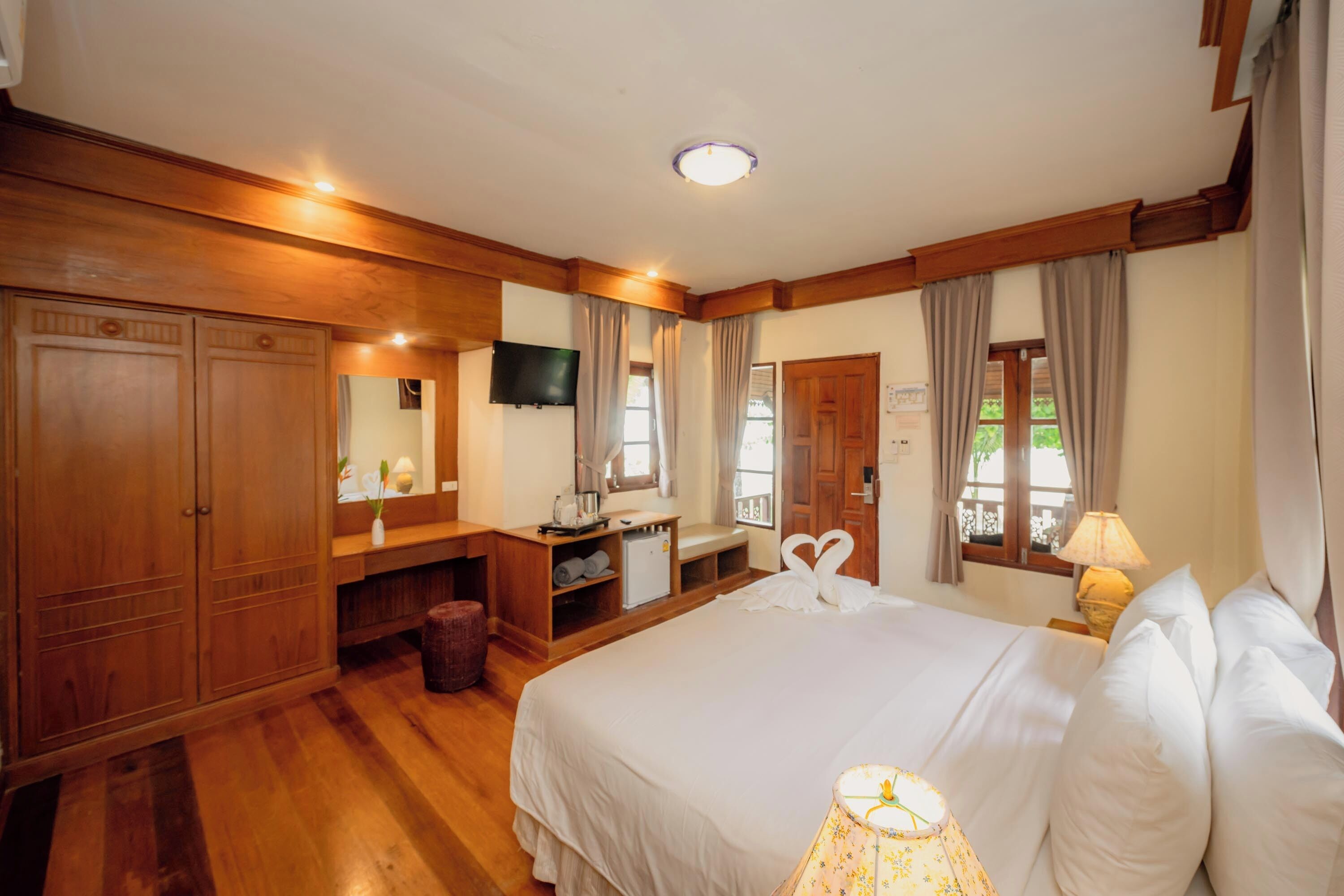 A hotel room with a large bed, wooden wardrobe, a desk with a chair, a television, and a window with curtains.