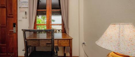 A room with a wooden door, a window with curtains, a table, a chair, and a lamp.