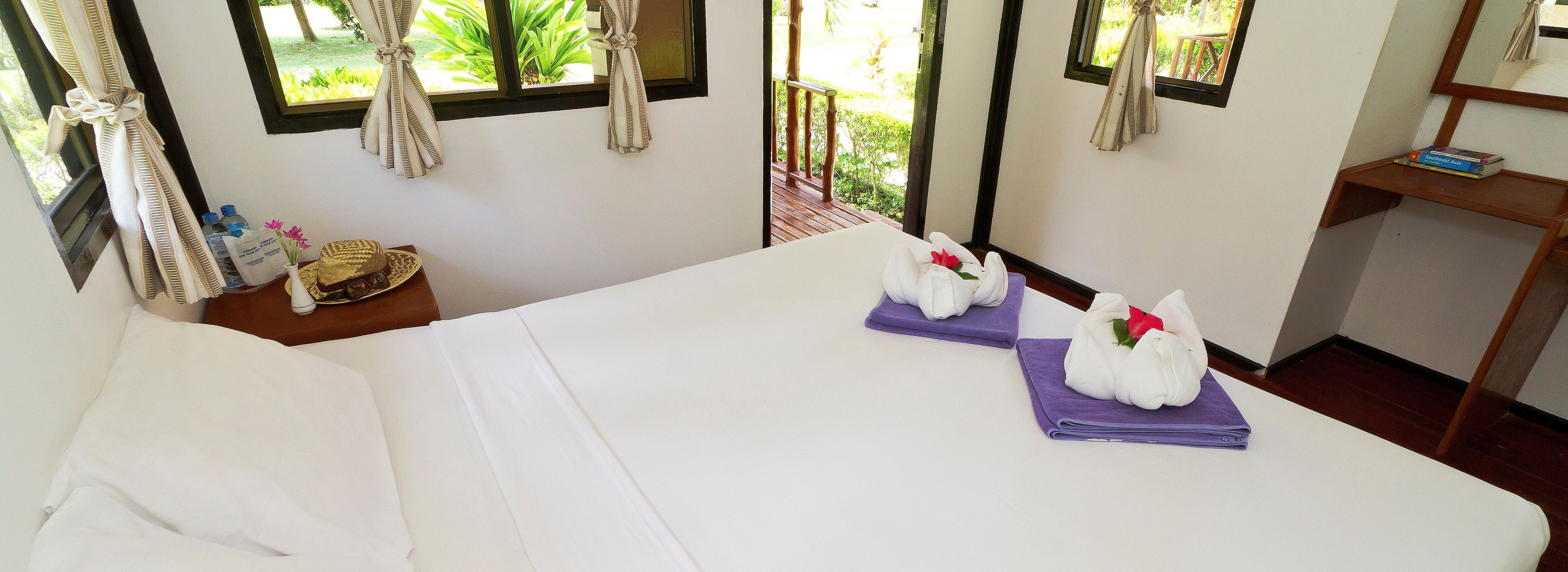 Una habitación de hotel con una cama, una mesita con artículos de aseo y un ventanal con cortinas.