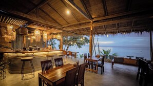 An outdoor restaurant with a bar, wooden tables and chairs, and a view of the sea. - Long Bay Resort (Ko Pha-ngan)