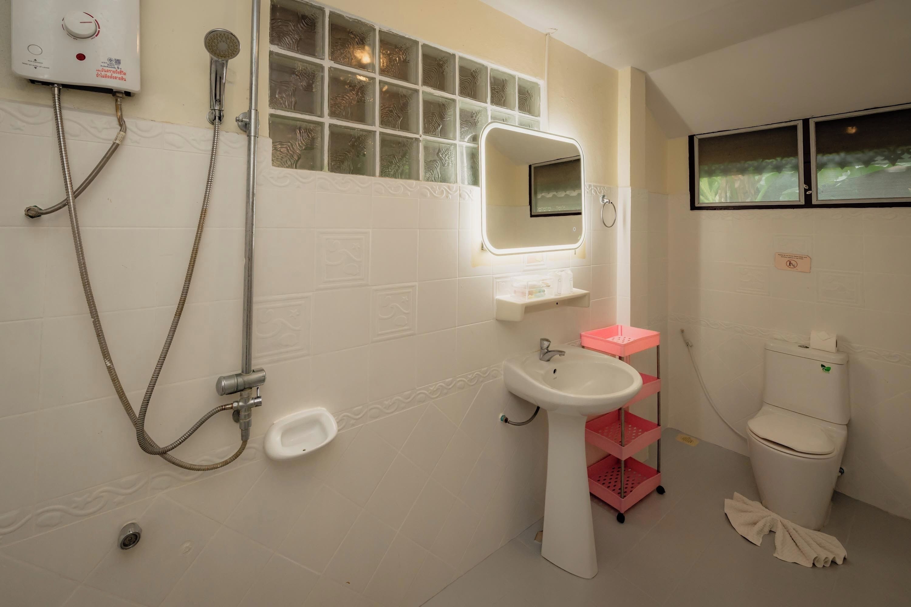 A bathroom with a shower, sink, toilet, and a window with frosted glass.