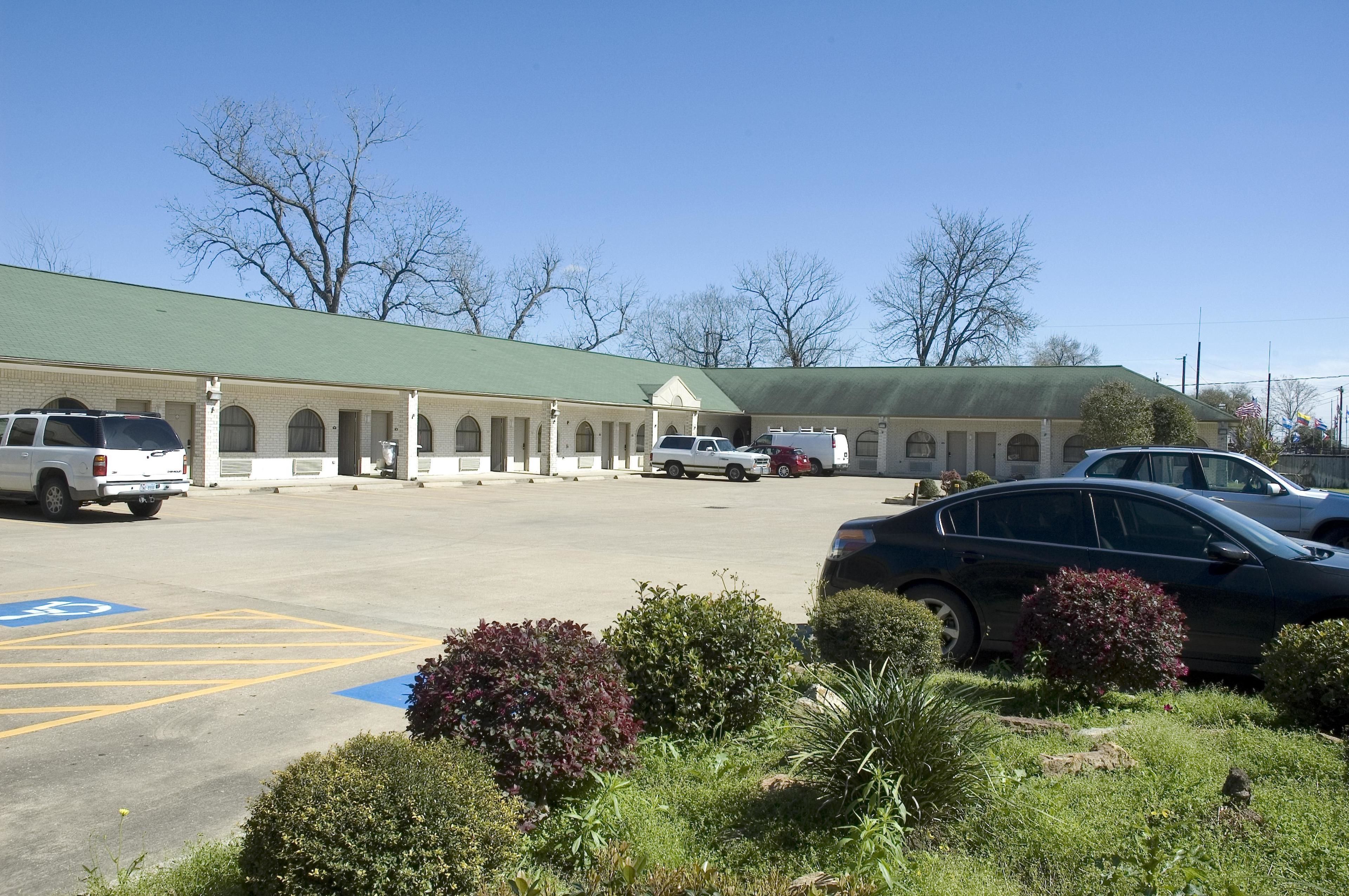 A motel with a row of rooms, a parking lot, and a green roof.