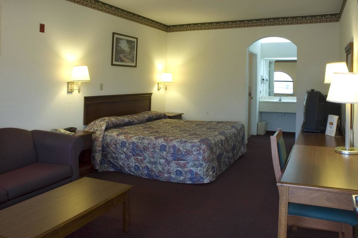 A hotel room with a bed, a sofa, a desk, and two wall-mounted lamps.