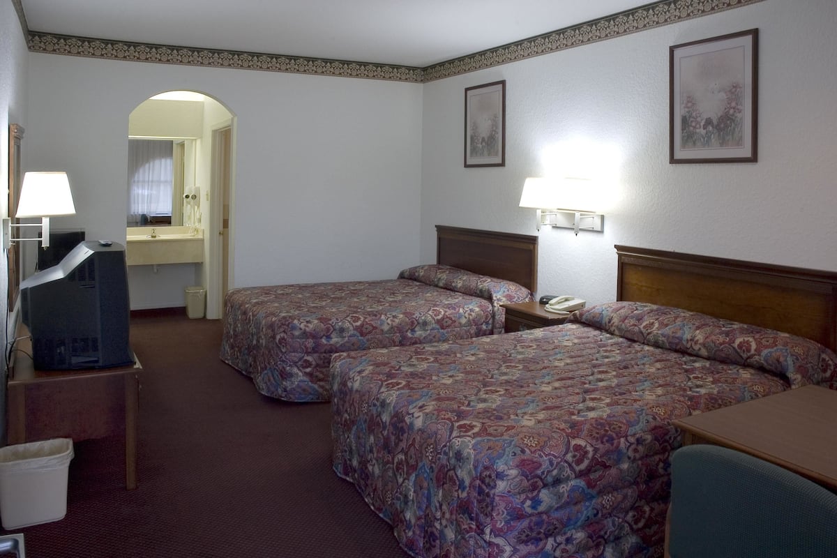 A hotel room with two beds, a desk, a chair, a TV, and a bathroom visible through an archway.