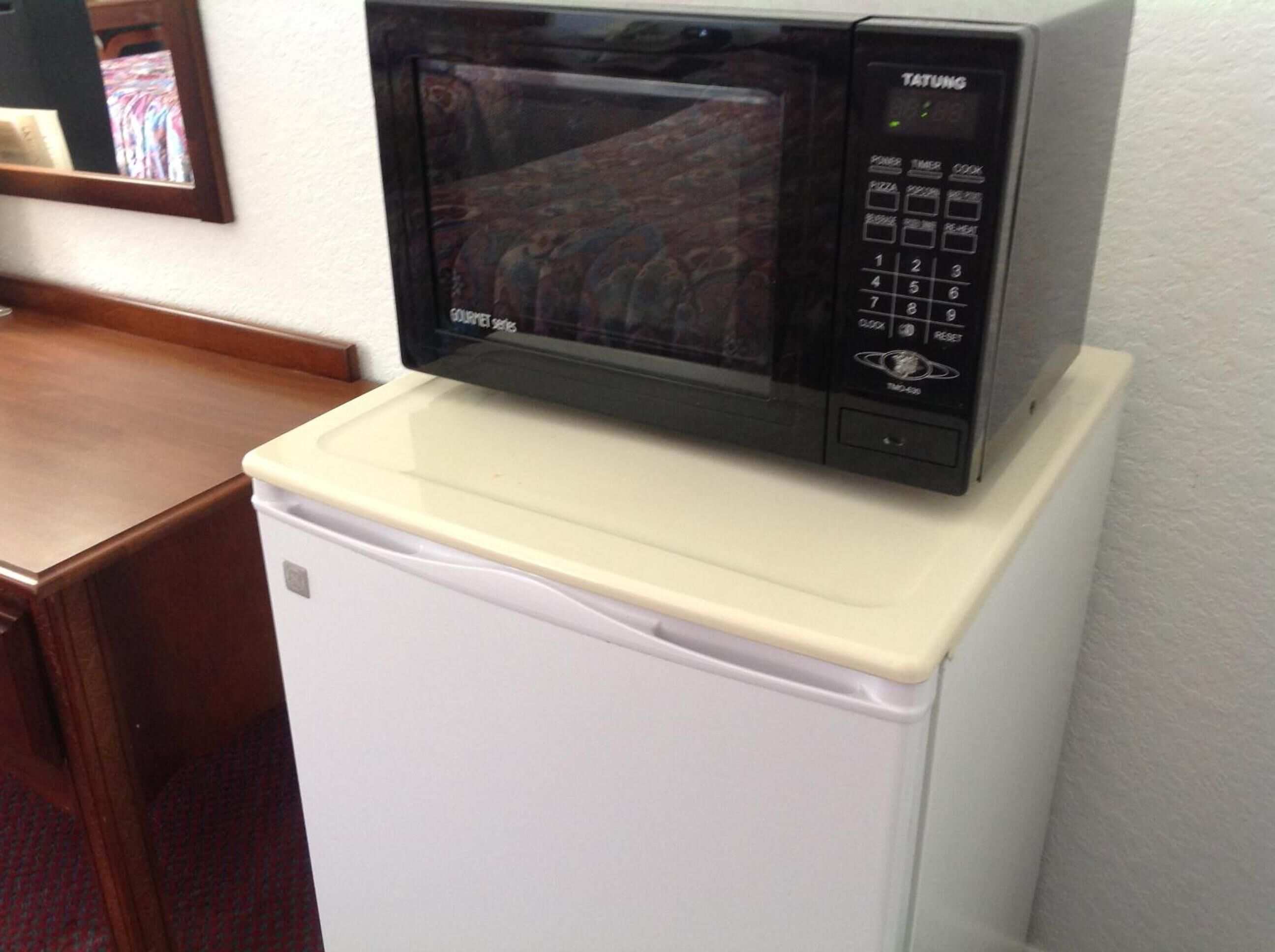 A microwave on top of a white refrigerator in a room with a wooden table and a mirror on the wall.