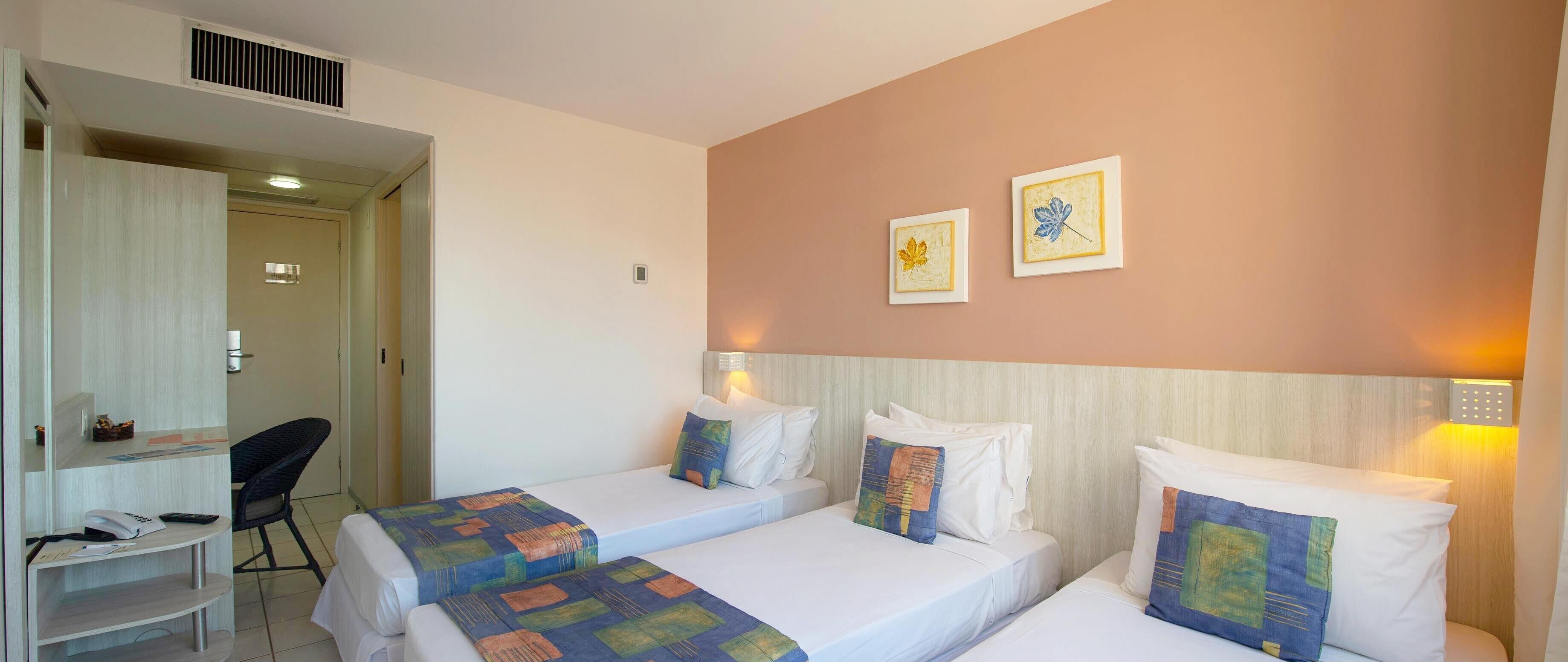 Ein Hotelzimmer mit zwei Einzelbetten, einem Schreibtisch mit Stuhl und zwei gerahmten Bildern an der Wand.