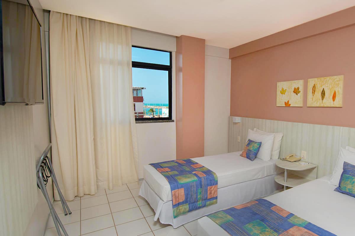 Habitación de hotel con dos camas, televisión, ventana con vistas y cuadros en la pared.