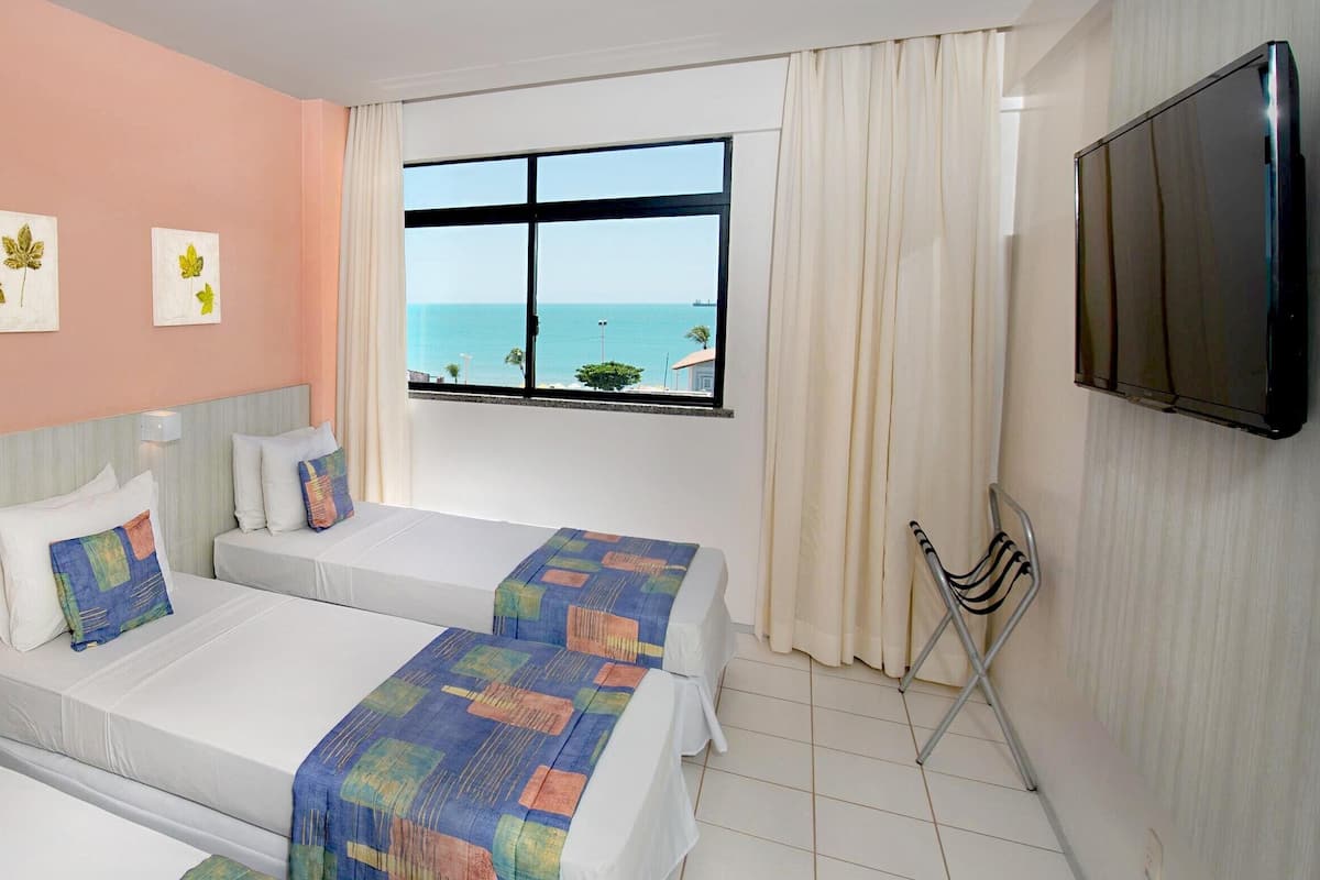 Habitación de hotel con dos camas, televisión y ventana con vista al mar.