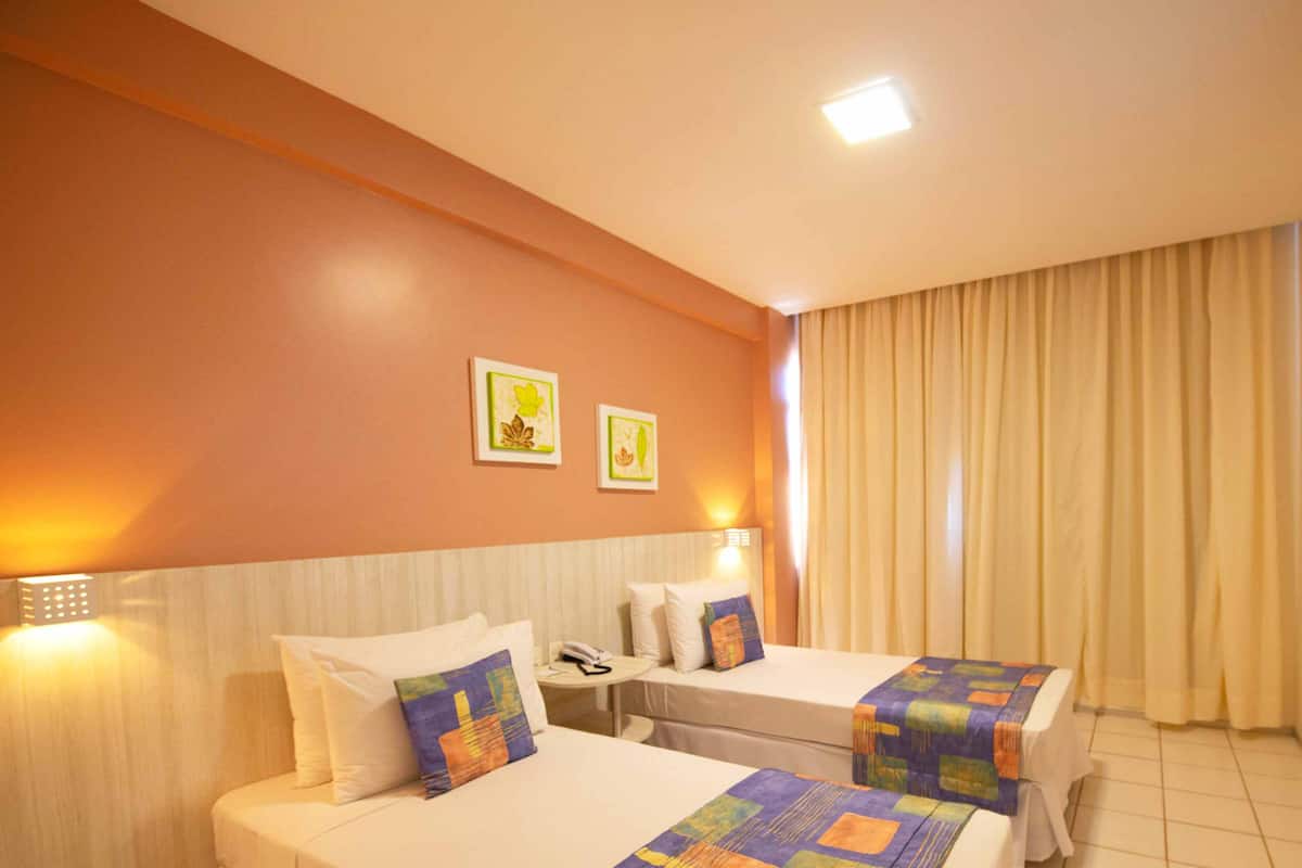 Una habitación de hotel con dos camas, un televisor en la pared y una mesita con un teléfono.