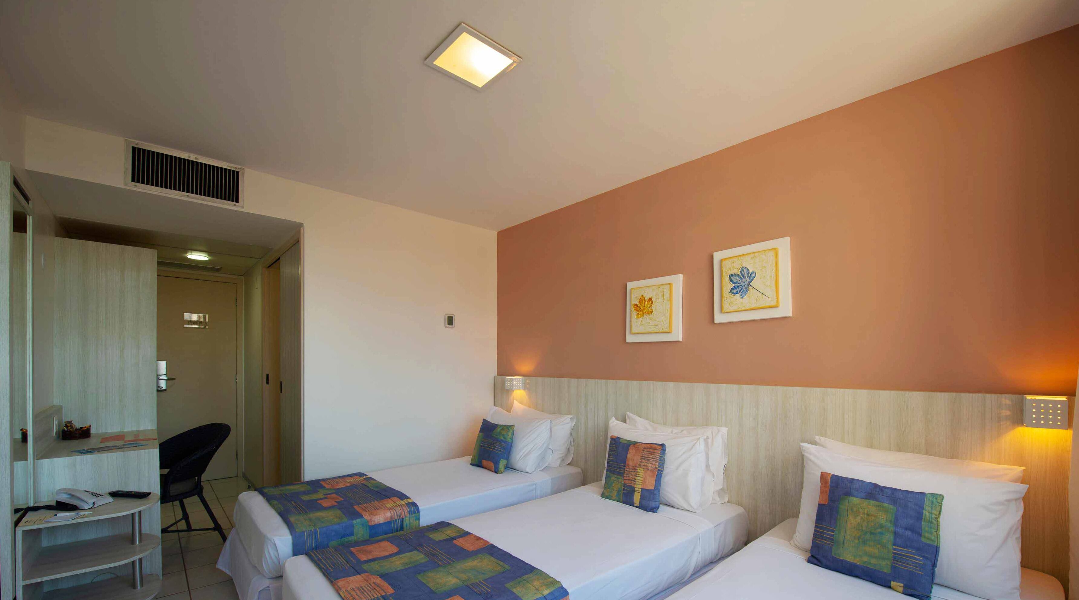 Quarto de hotel com duas camas de solteiro, uma escrivaninha com cadeira e uma kitchenette pequena.