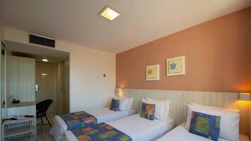Quarto de hotel com duas camas de solteiro, uma escrivaninha com cadeira e uma kitchenette pequena.