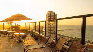 A balcony with wicker chairs and a table, overlooking a coastal view with a bridge and buildings. - Maredomus Hotel (Fortaleza)