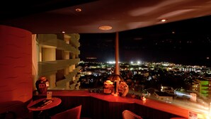 A high-rise hotel room with a city view, a red accent wall, and a small table with a chair. - Okinawa Grand Mer Resort (Okinawa)