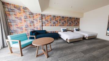 Une chambre d’hôtel avec un canapé, deux lits simples, une table ronde et un mur décoré de motifs.