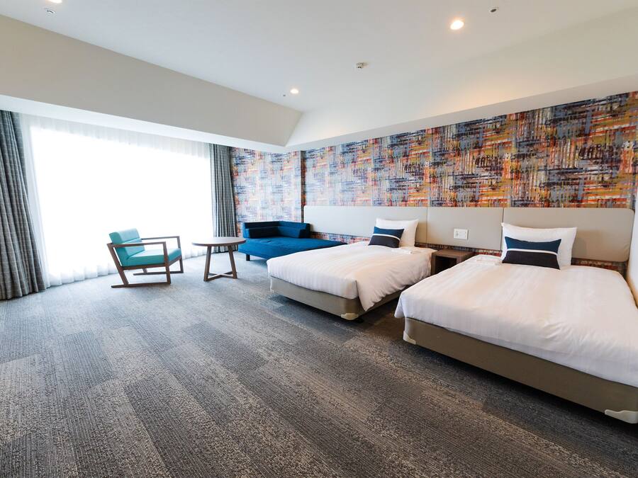 A hotel room with two beds, a sofa, a chair, and a large window.