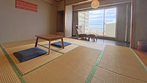 A traditional Japanese room with tatami flooring, a low wooden table, a cushioned bench, and a large window offering a city view. - Okinawa Grand Mer Resort (Okinawa)
