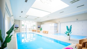 An indoor swimming pool with clear blue water, surrounded by lounge chairs and potted plants. - Okinawa Grand Mer Resort (Okinawa)