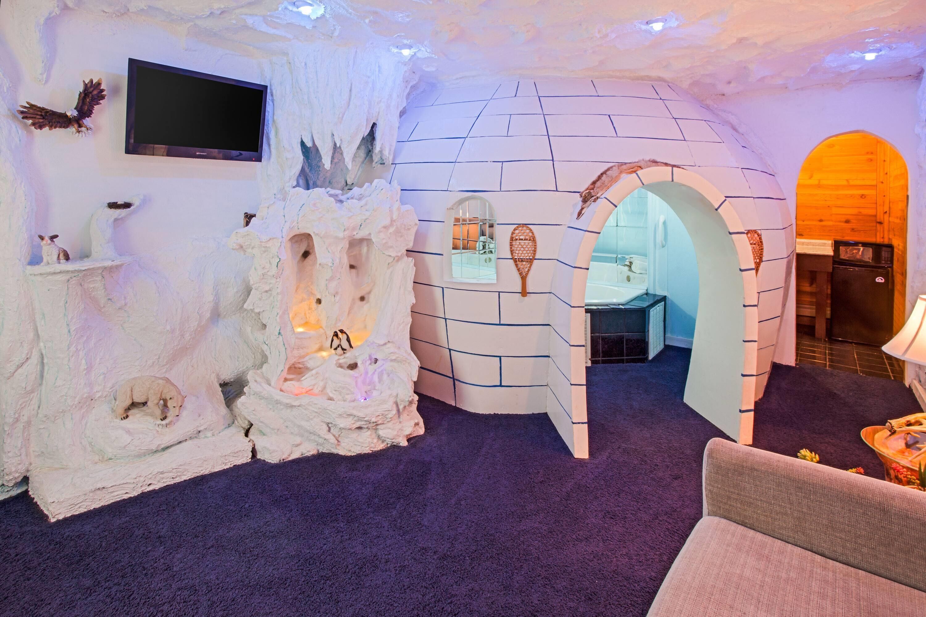 Une pièce en forme d’igloo, équipée d’un téléviseur, d’une cheminée et d’une arche en bois qui mène à une autre pièce.