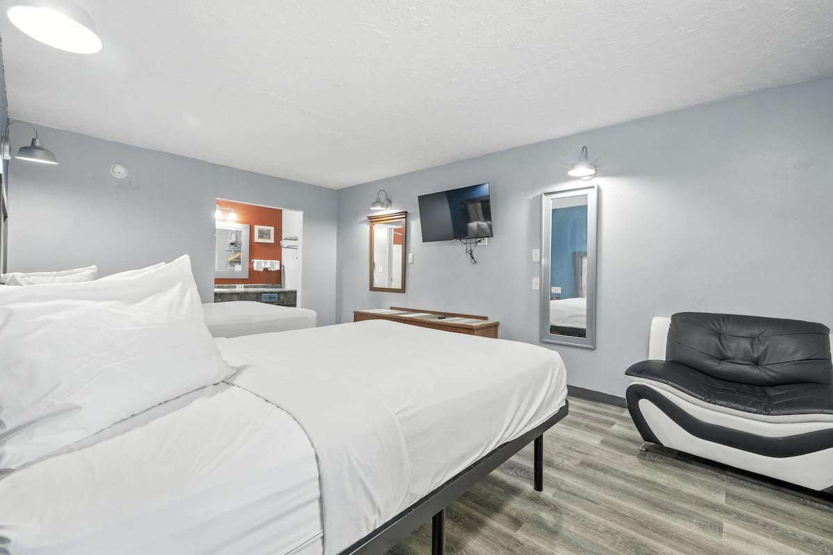 A hotel room with a bed, a chair, a TV, and a mirror.