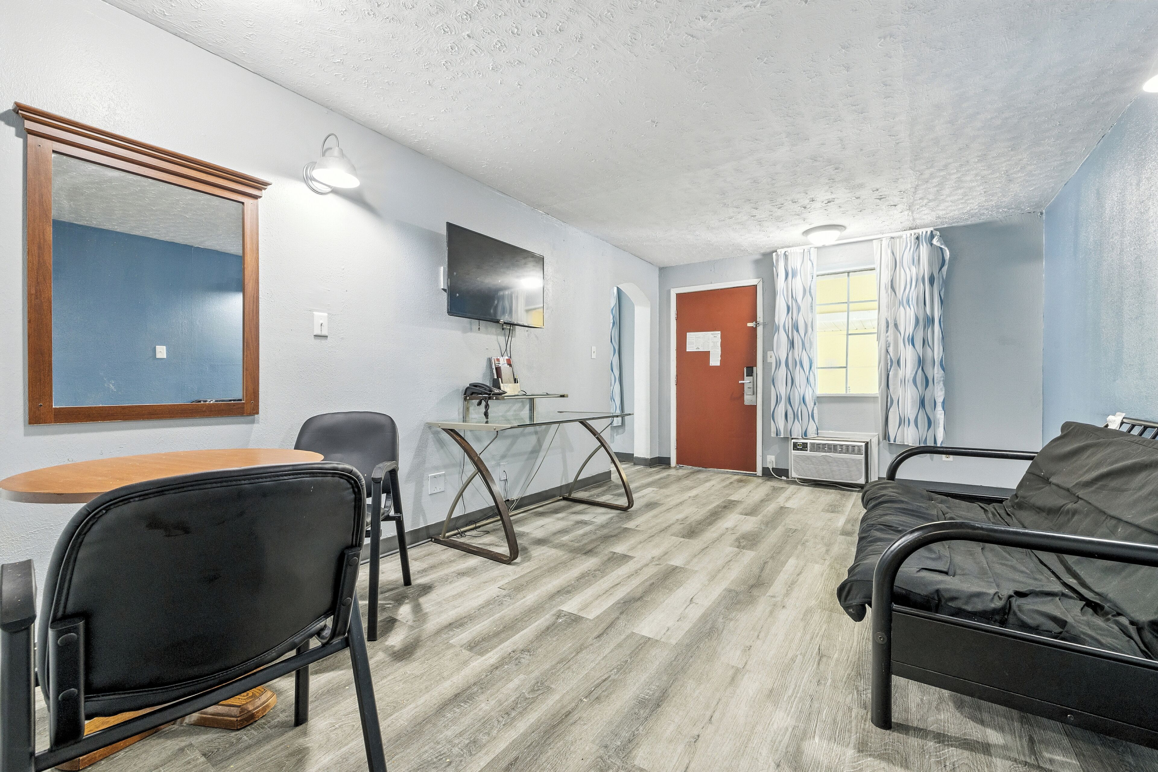 A room with a bed, a desk with a chair, a TV mounted on the wall, and a window with curtains.