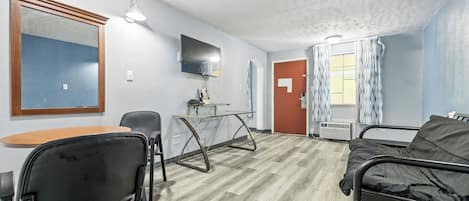 A room with a bed, a desk with a chair, a TV mounted on the wall, and a window with curtains.