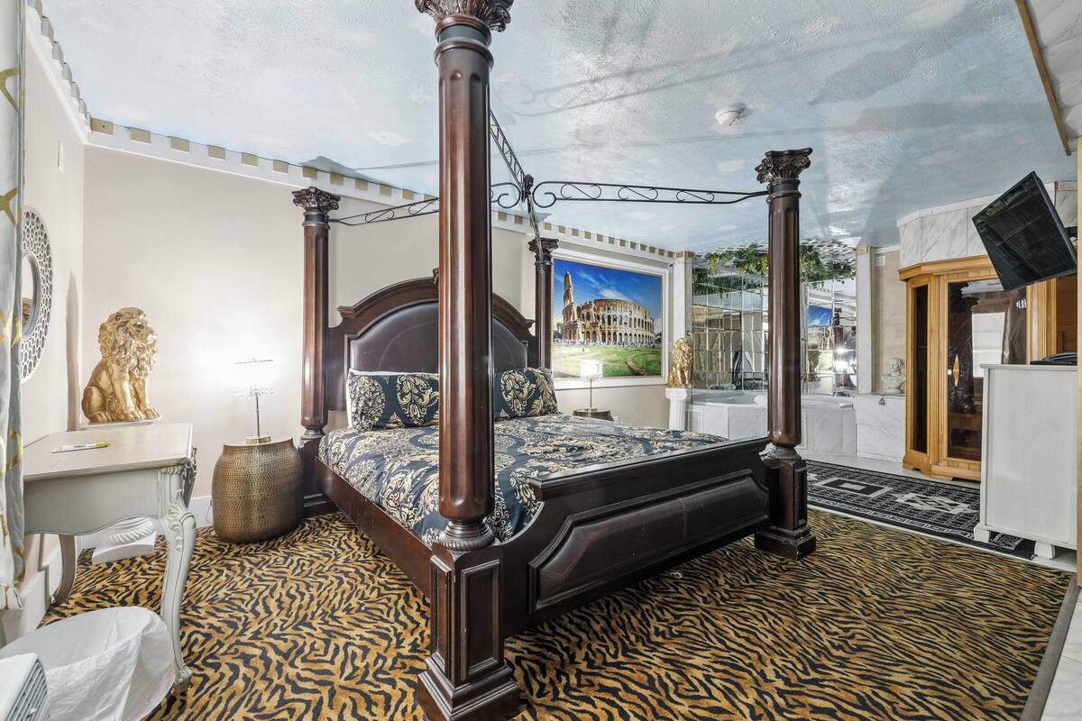 A four-poster bed with a view of the Colosseum through a large window.