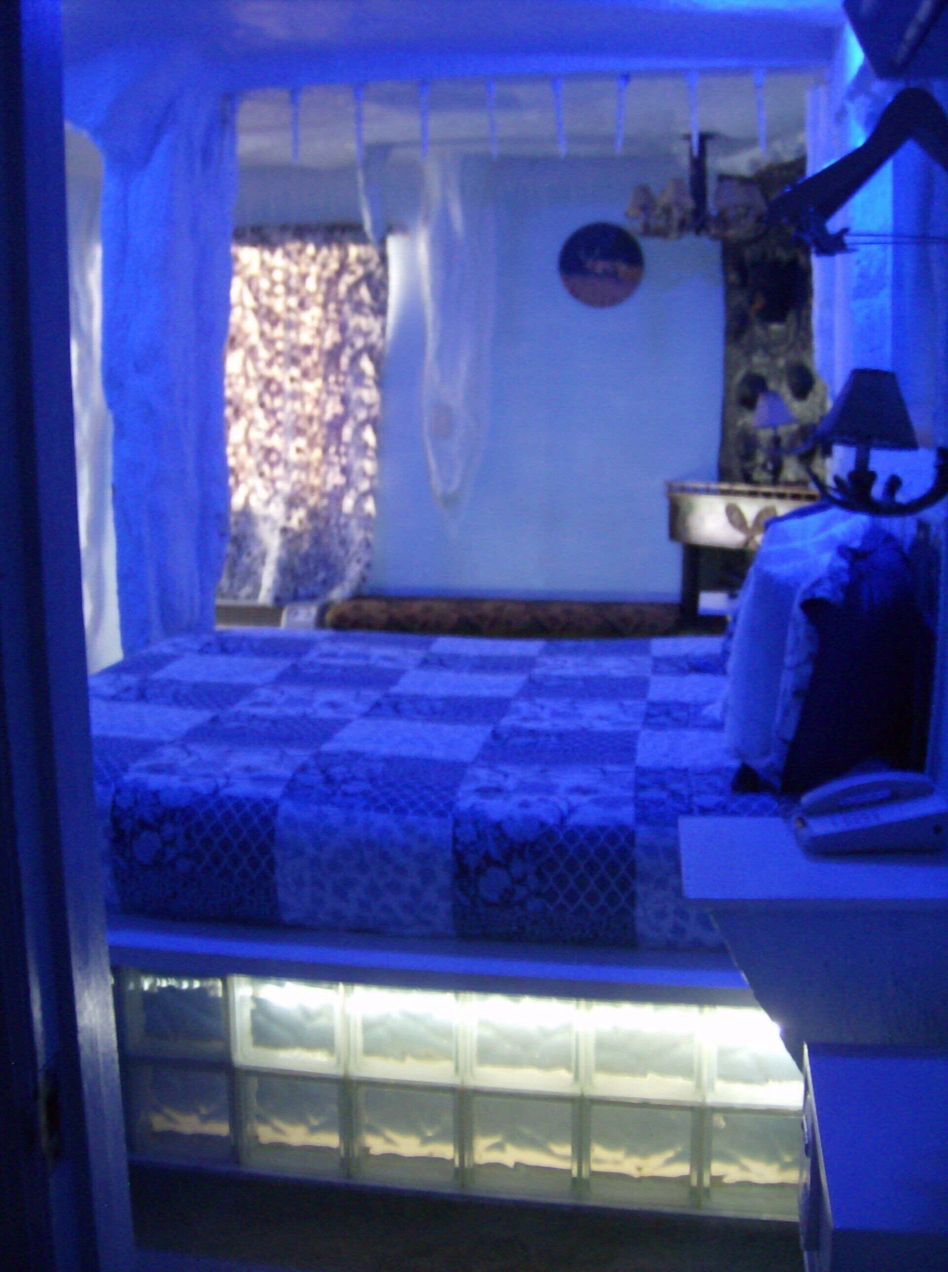A bedroom with a checkered bedspread, a bedside table with a lamp, and a window with curtains.