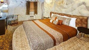 Una habitación con pared de piedra, una cama con colcha de estampado de cebra, un sillón con estampado de cebra y una pequeña mesa con una lámpara.