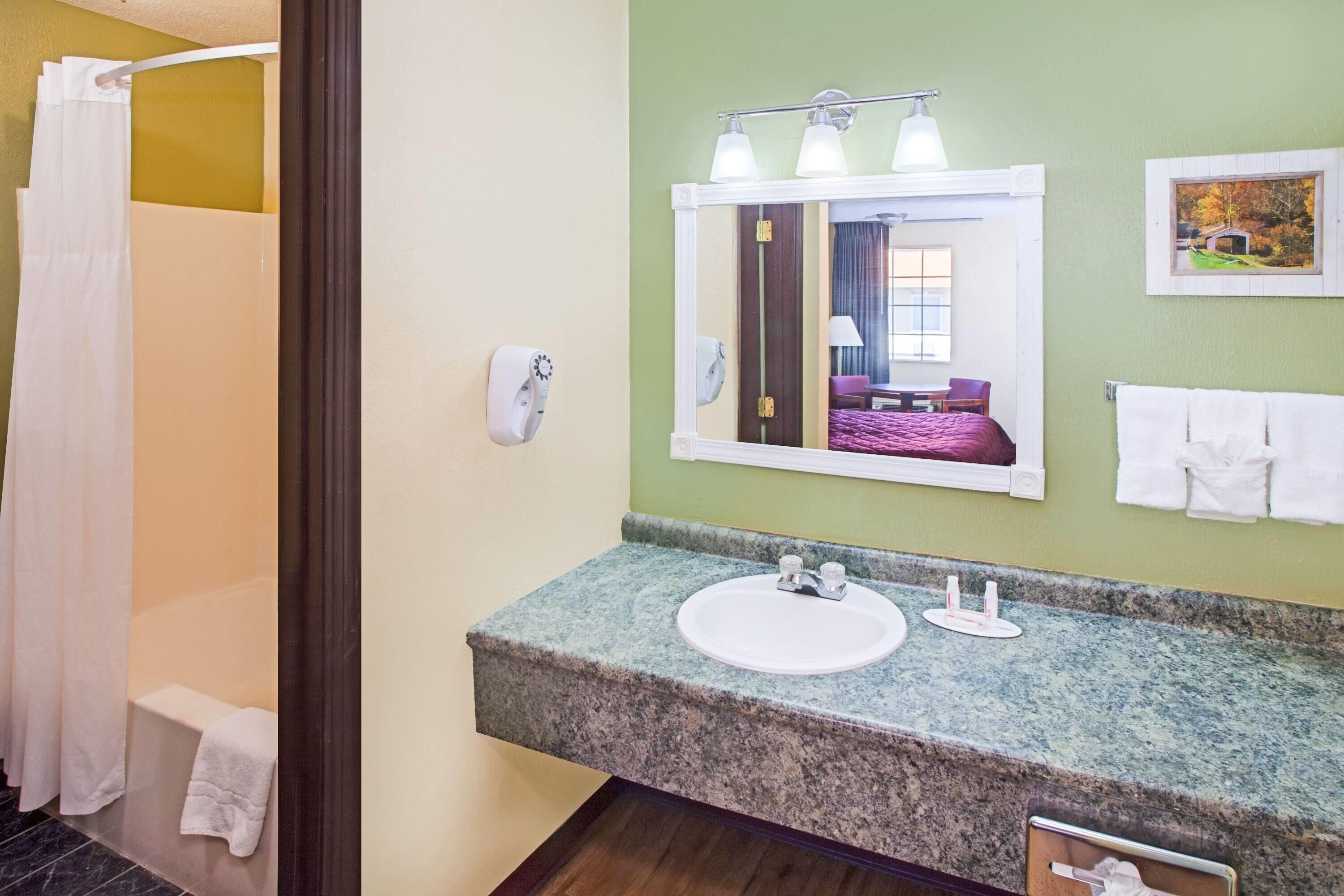 Un baño con encimera de granito, un lavabo, un espejo, un perchero para toallas y una cortina de ducha.