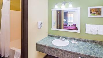 Un baño con encimera de granito, un lavabo, un espejo, un perchero para toallas y una cortina de ducha.