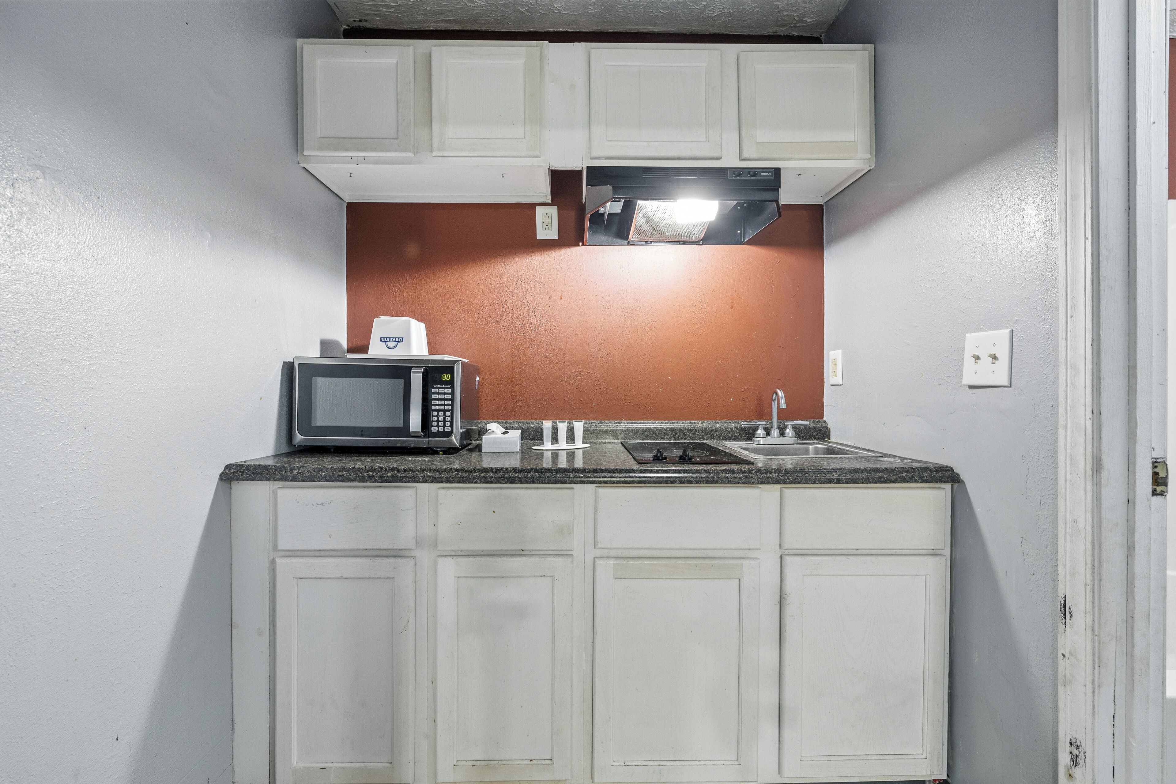 Una cocina compacta con gabinetes blancos, microondas, pileta y estufa.