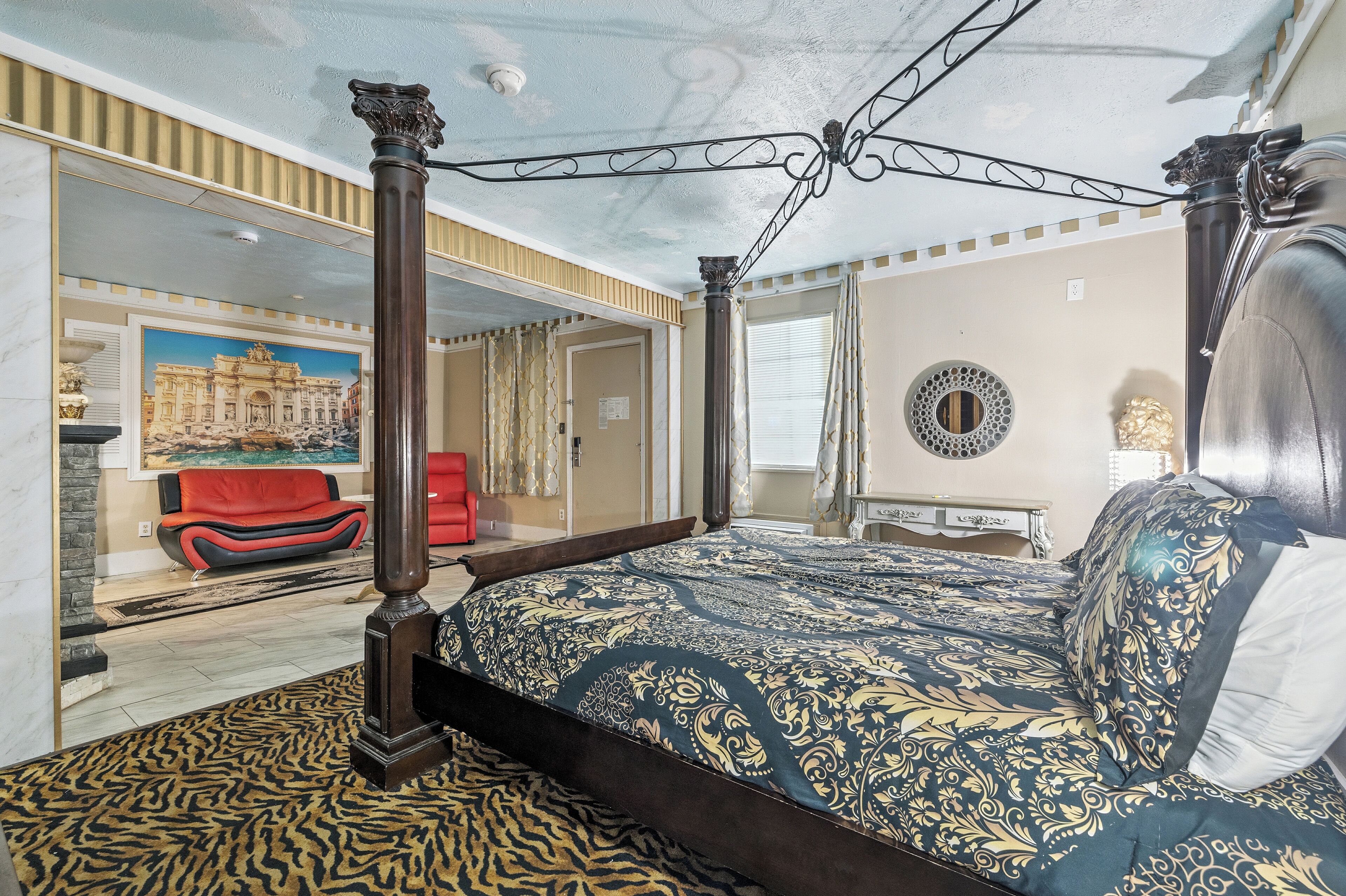 Ein Himmelbett mit gemustertem Überwurf, ein rotes Sofa und ein Spiegel an der Wand.