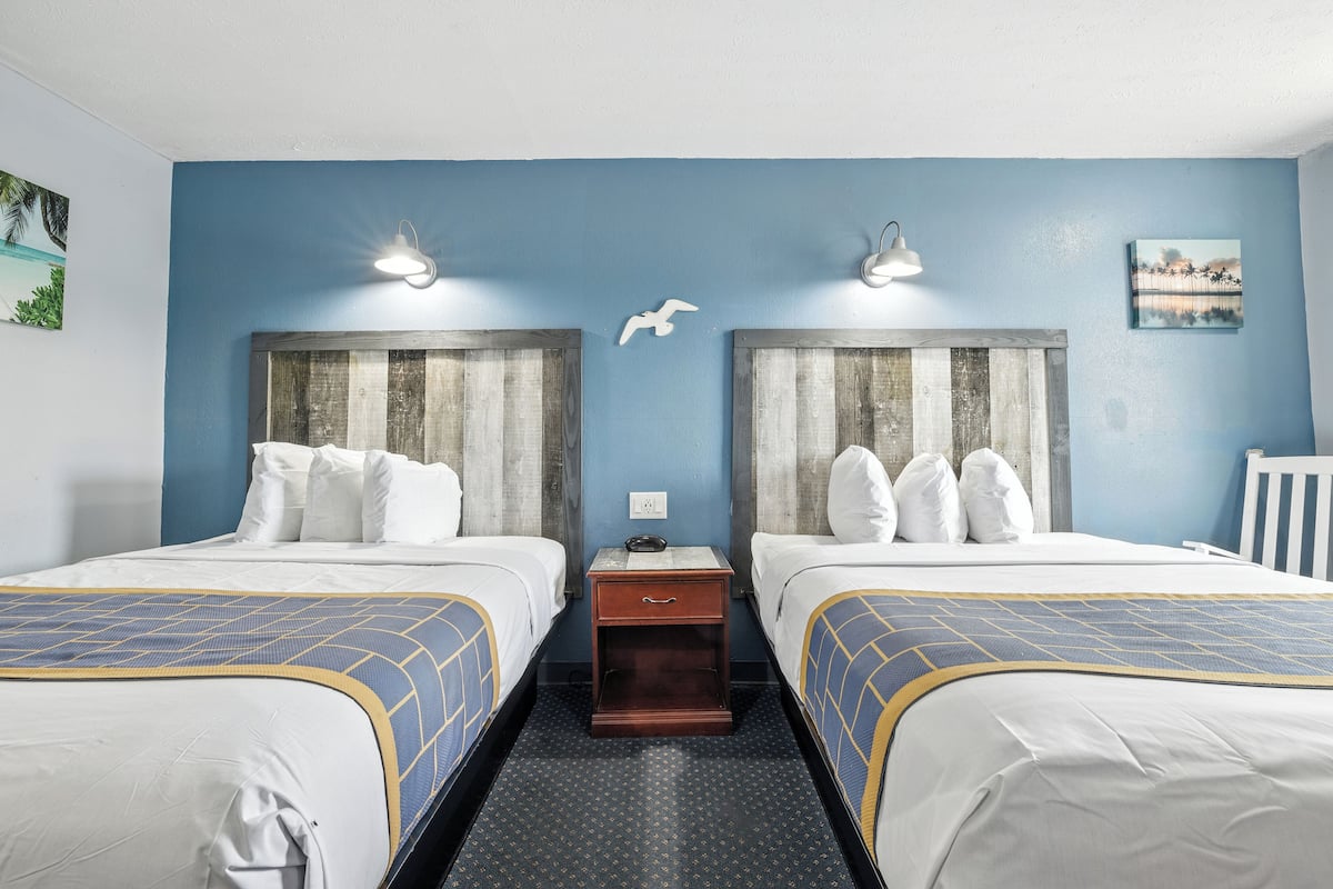 A hotel room with two beds, a nightstand, and a small table.