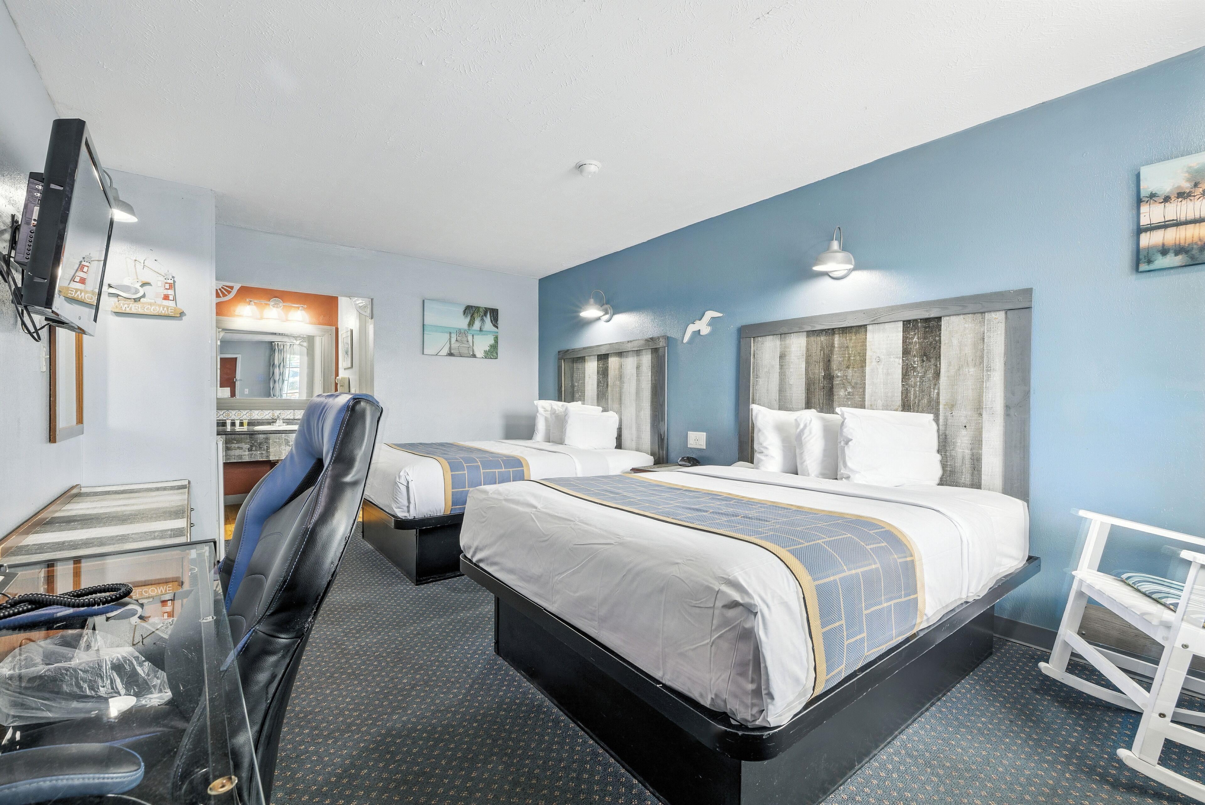 A hotel room with two beds, a desk, a chair, and a TV.