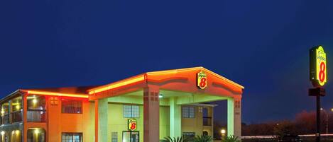 Un motel con una gasolinera, que presenta un edificio de dos pisos, un área de estacionamiento techada y un letrero de neón.