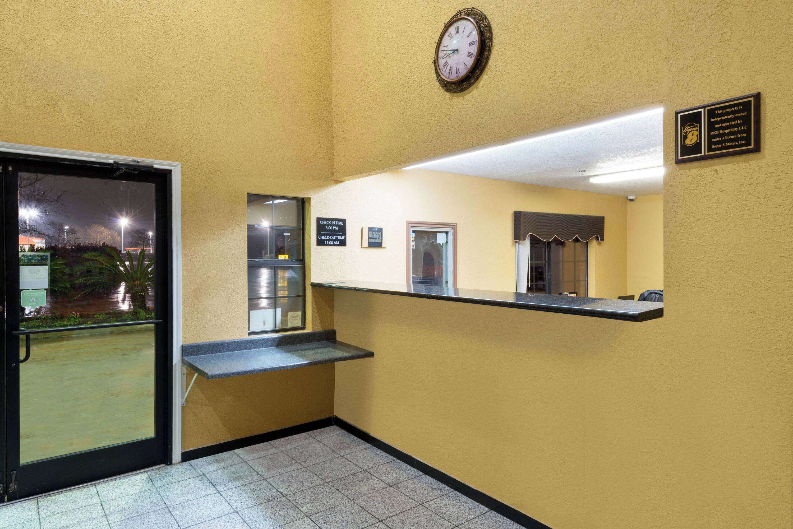 Ein Empfangsbereich mit einer Uhr, einem Check-in/Check-out-Schild und einer Rezeption.