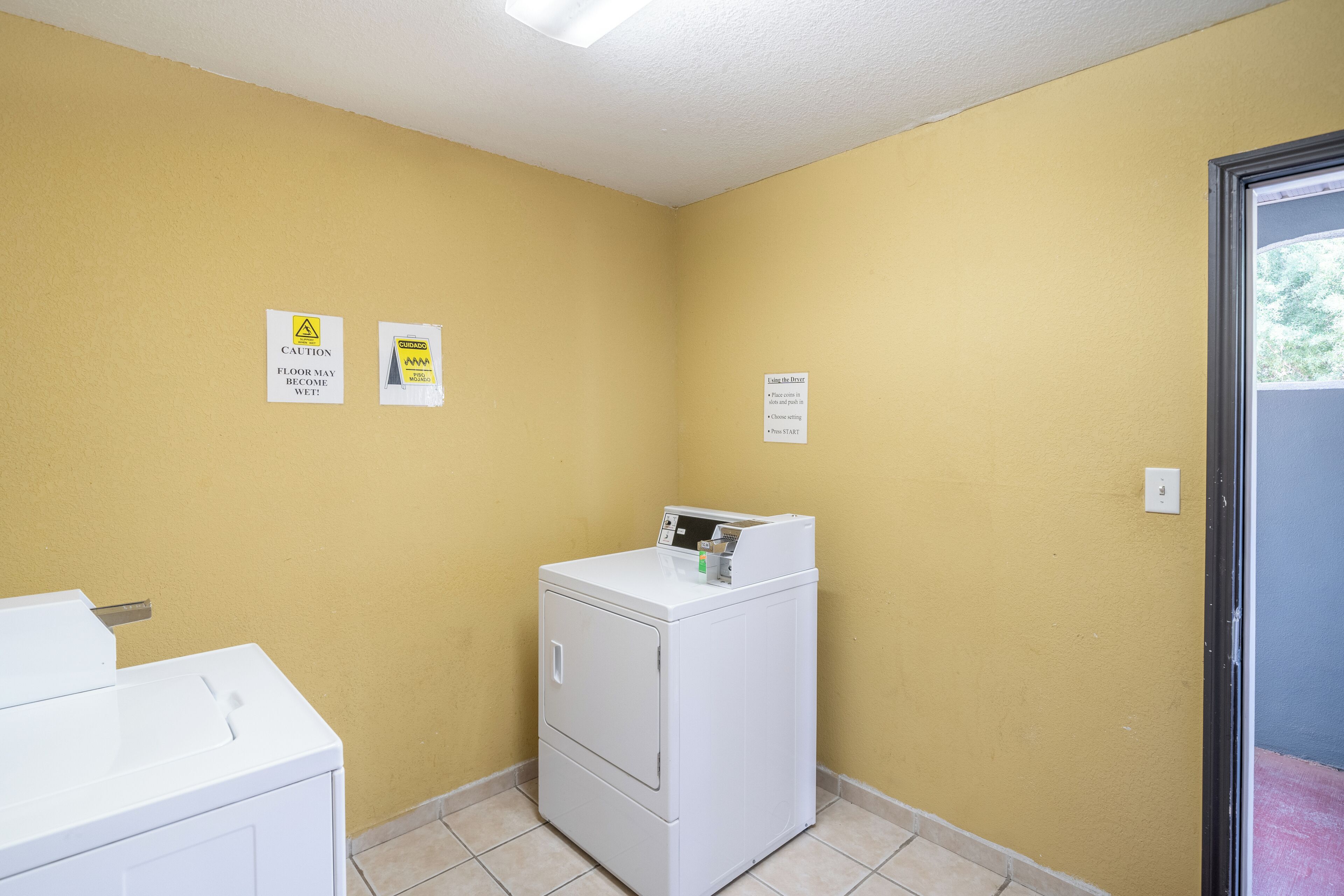 A laundry room with a washing machine and dryer, yellow walls, and caution signs.