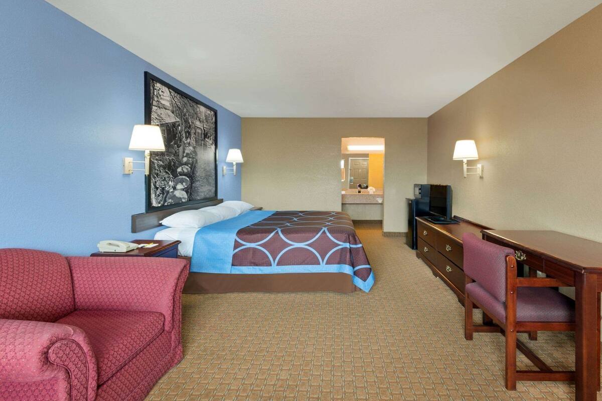 Ein Hotelzimmer mit einem Bett, einem Schreibtisch, einem Sessel, einem Fernseher und einem durchgegangene Tür erkennbaren Badezimmer.