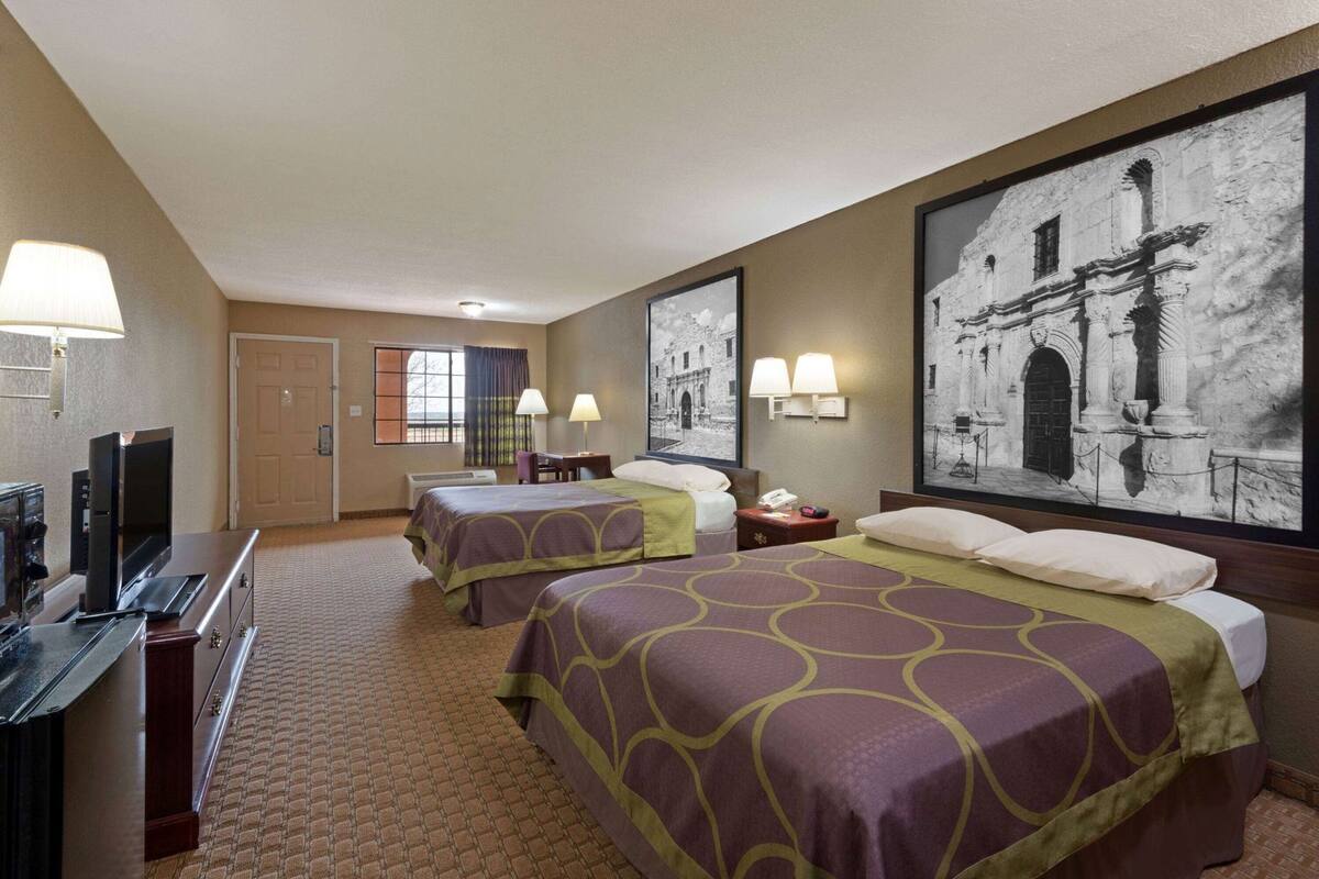 Ein Hotelzimmer mit zwei Betten, einem Fernseher, einem Schreibtisch und einem großen, gerahmten Bild an der Wand.