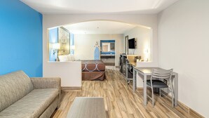 A modern hotel room with a living area, a dining table, and a kitchenette.