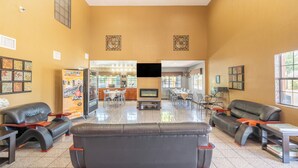 A spacious lobby with leather sofas, a TV screen, and a dining area with tables and chairs.