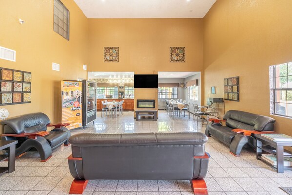 A spacious lobby with leather sofas, a TV screen, and a dining area with tables and chairs.