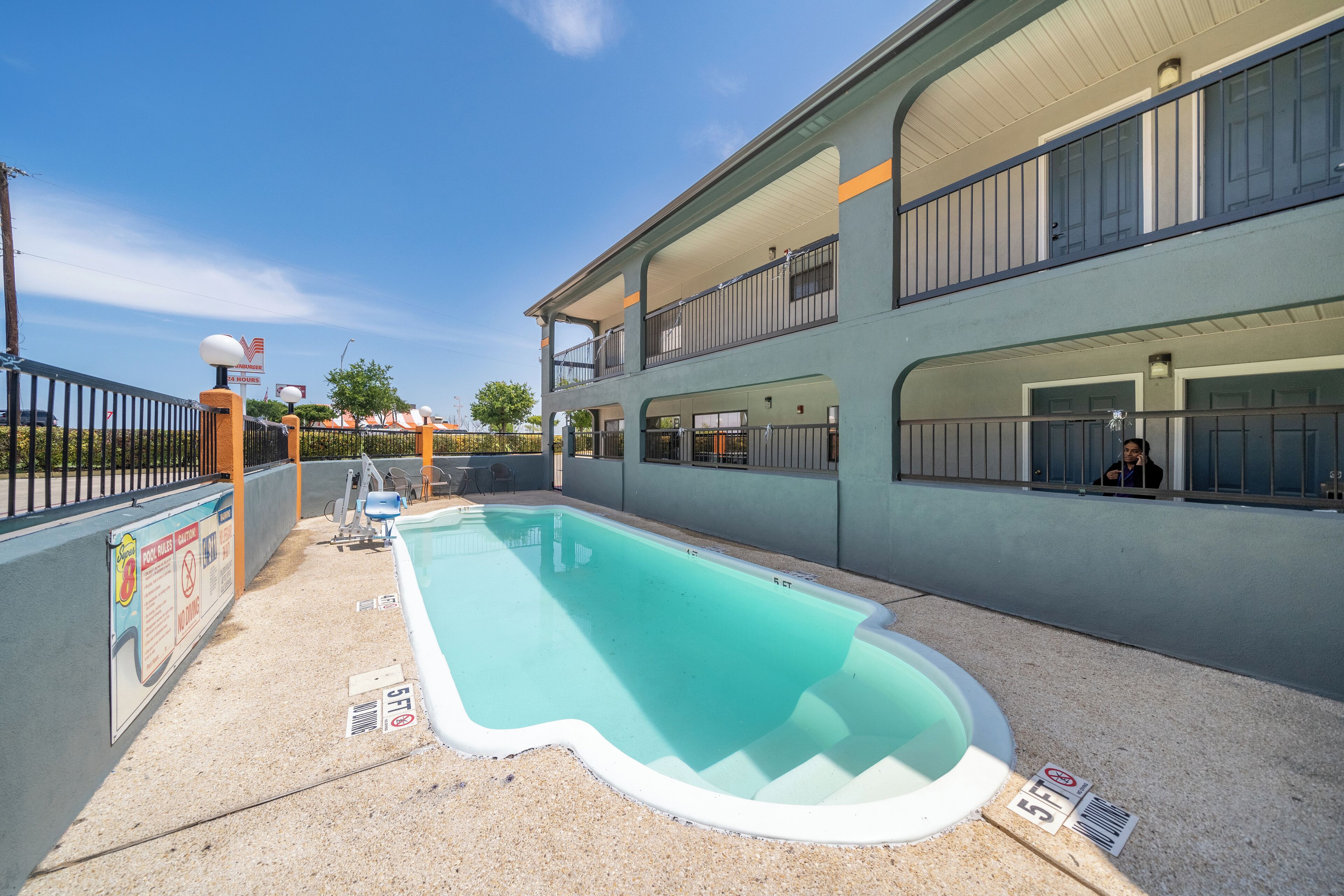A swimming pool area with a two-story building, a fenced patio, and a clear sky.