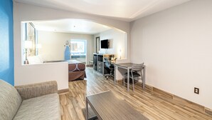 A modern hotel room with a wooden floor, a sofa, a desk, and a TV.